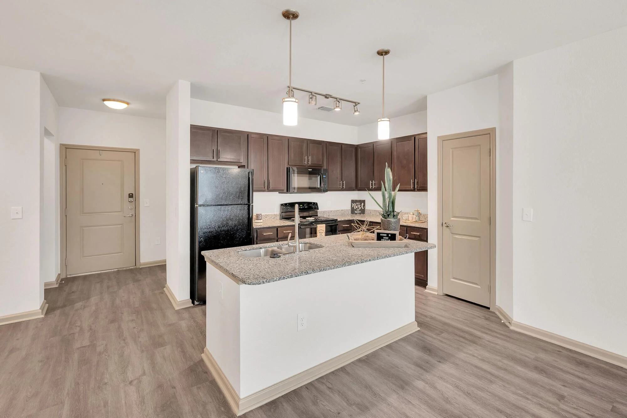 Modern kitchen with dark wood cabinets, granite island, stainless appliances, and wood-style flooring.