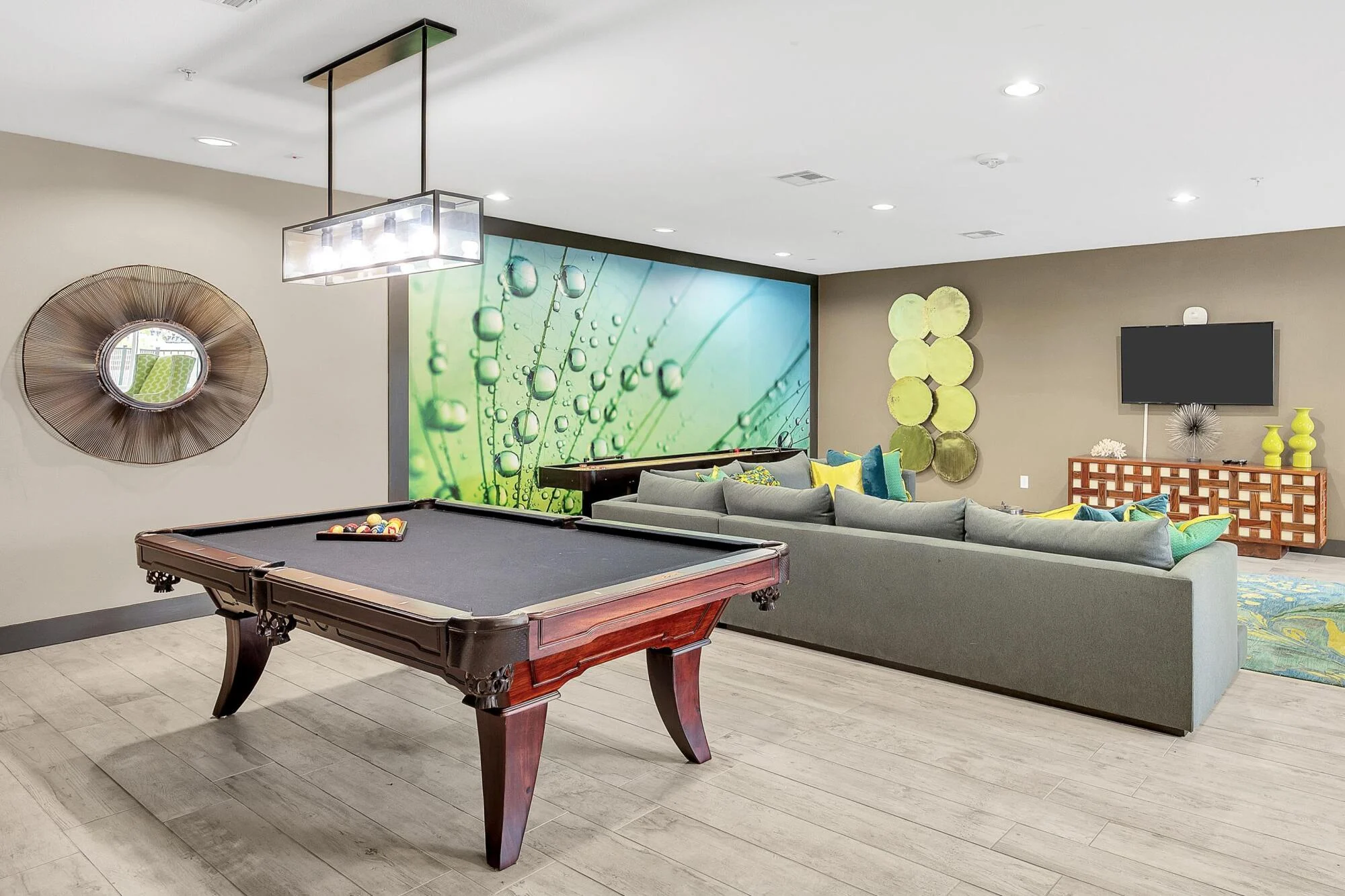 Modern lounge with a pool table, sectional sofa, TV, and vibrant green wall art and decor accents.