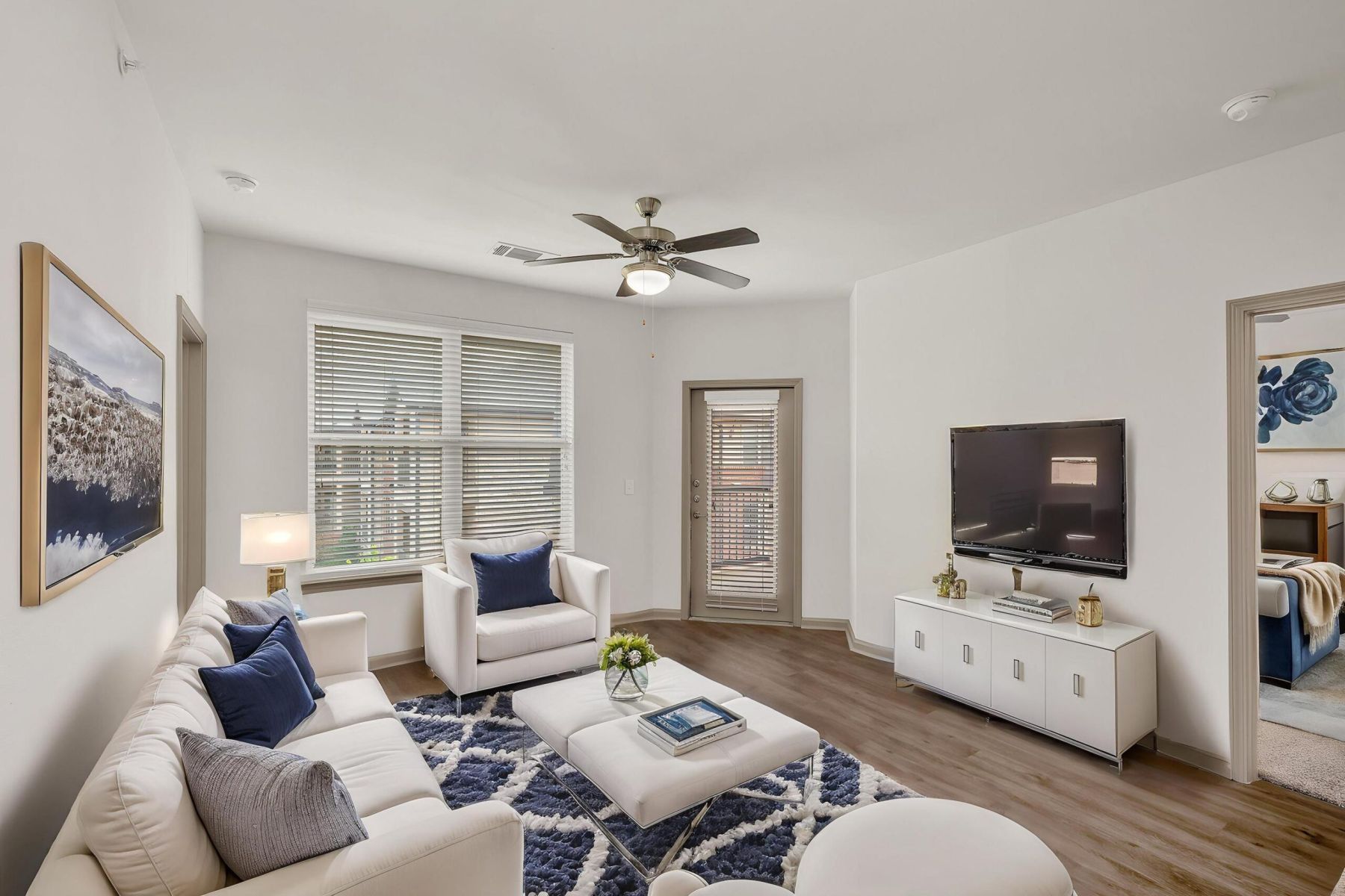 Empty room with wood floors, ceiling fan, and sliding glass door leading to a patio with vertical blinds at Apex West Midown.
